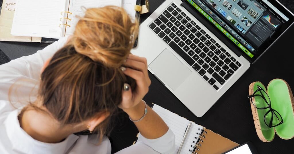 pexels-photo-313690-313690 Overhead view of a stressed woman working at a desk with a laptop, phone, and notebooks.